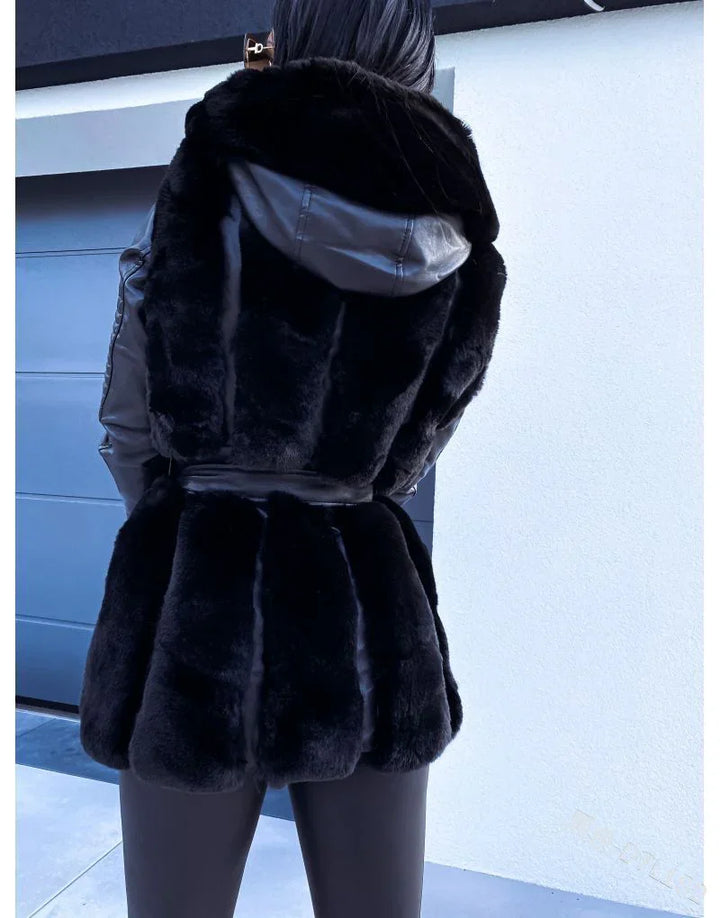 Back view of person wearing black faux fur coat with leather hood and sleeves against modern building