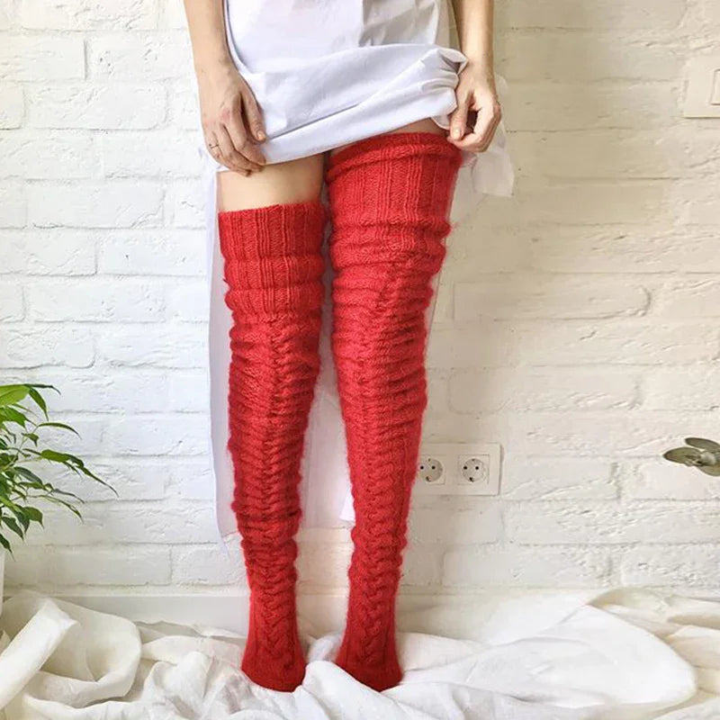 Person wearing bright red knitted thigh-high socks standing against white brick wall with plants nearby