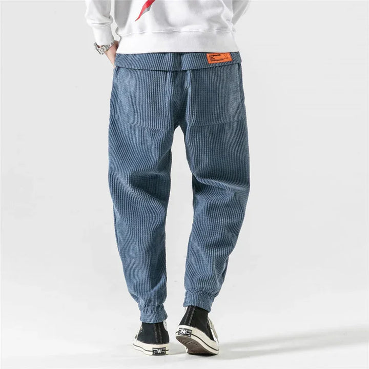 Rear view of a person wearing blue corduroy jogger pants with elastic cuffs and black high-top sneakers