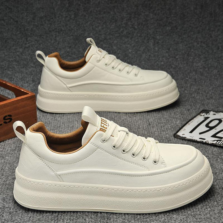 Pair of white leather lace-up sneakers with thick soles and brown inner lining on gray carpet