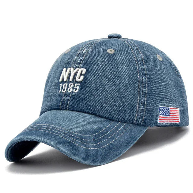 Blue denim baseball cap with white embroidered NYC 1985 on front and American flag patch on side