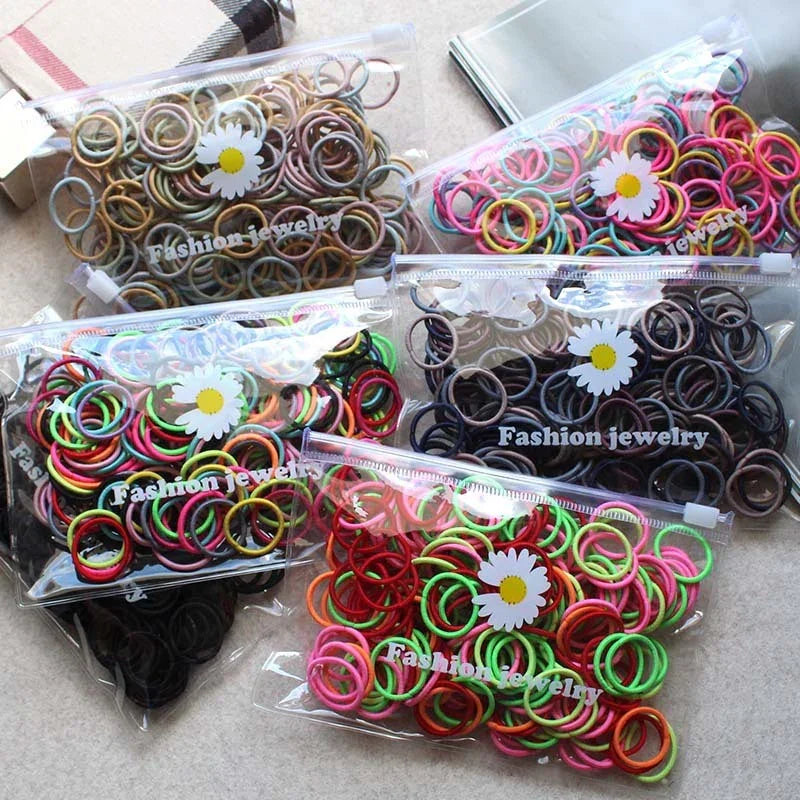 Five transparent zipper bags filled with colorful and neutral rubber hair ties labeled fashion jewelry