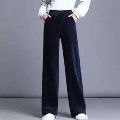 Person wearing black wide-leg pants with drawstring waist and white sneakers against gray background