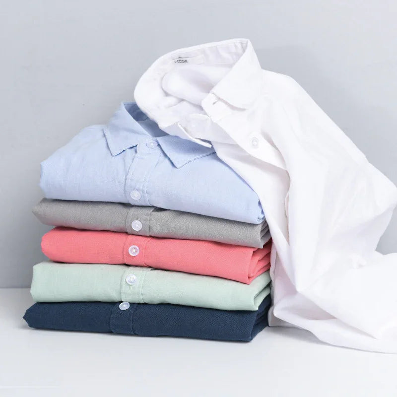 Stack of folded cotton polo shirts in navy, mint, coral, gray, light blue, and a white one draped over on white surface