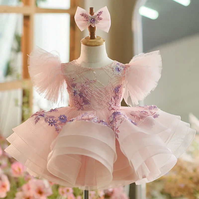 Pink toddler dress with ruffled tulle sleeves and floral embroidery on a dress form with matching bow