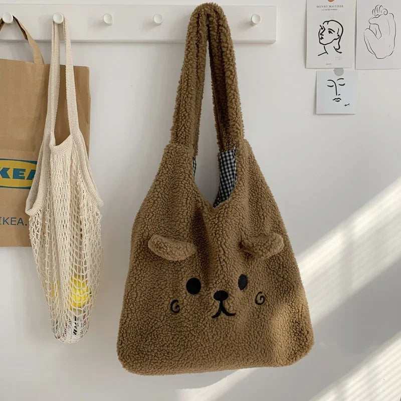 Brown teddy bear fleece tote bag hanging on white wall hook with net bag and IKEA paper bag nearby