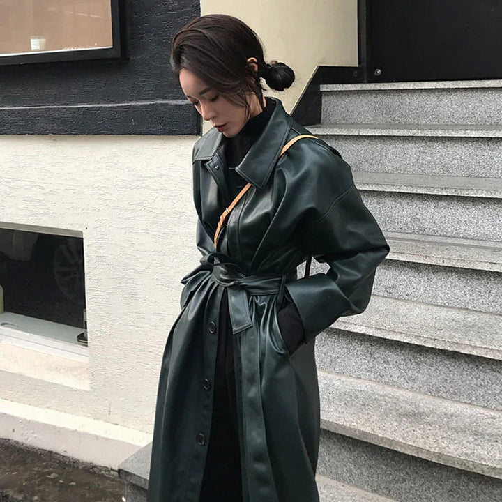Woman in a dark green belted leather trench coat standing near stone stairs outdoors