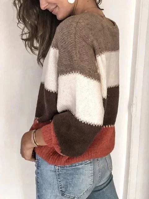 Woman wearing cozy striped knit sweater in brown, white, and rust shades with light blue jeans