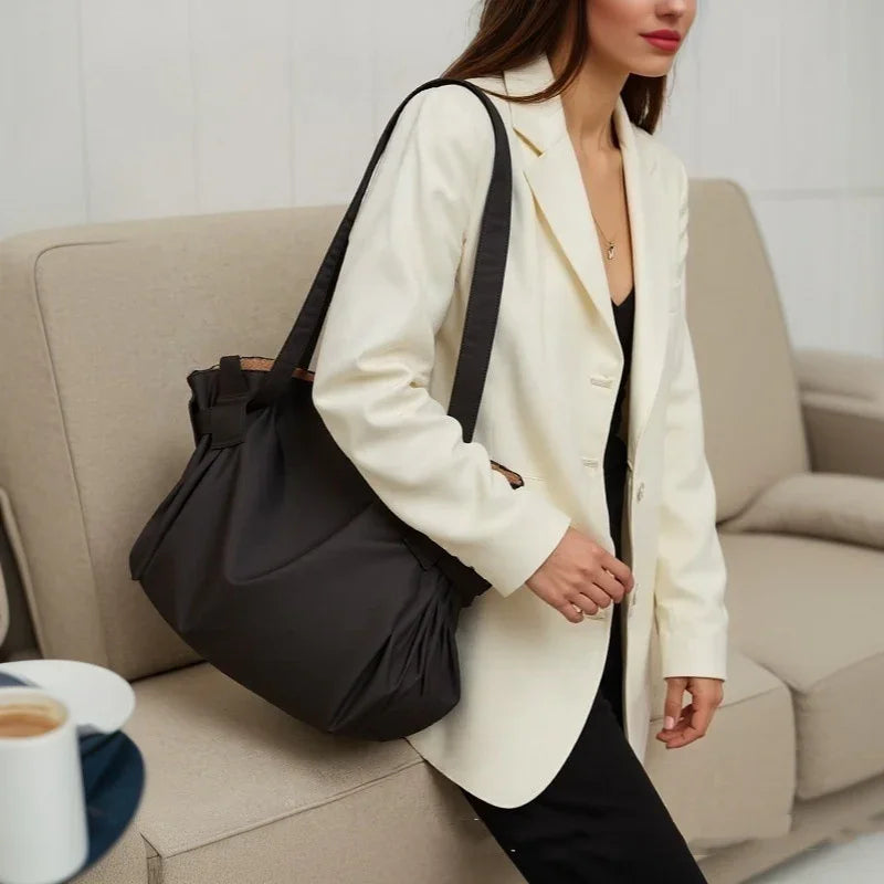 Woman wearing white blazer carrying black handbag while sitting on beige sofa in modern living room