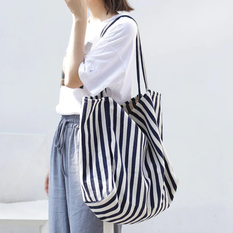 Woman wearing casual white t-shirt and gray pants carrying large navy and white striped tote bag
