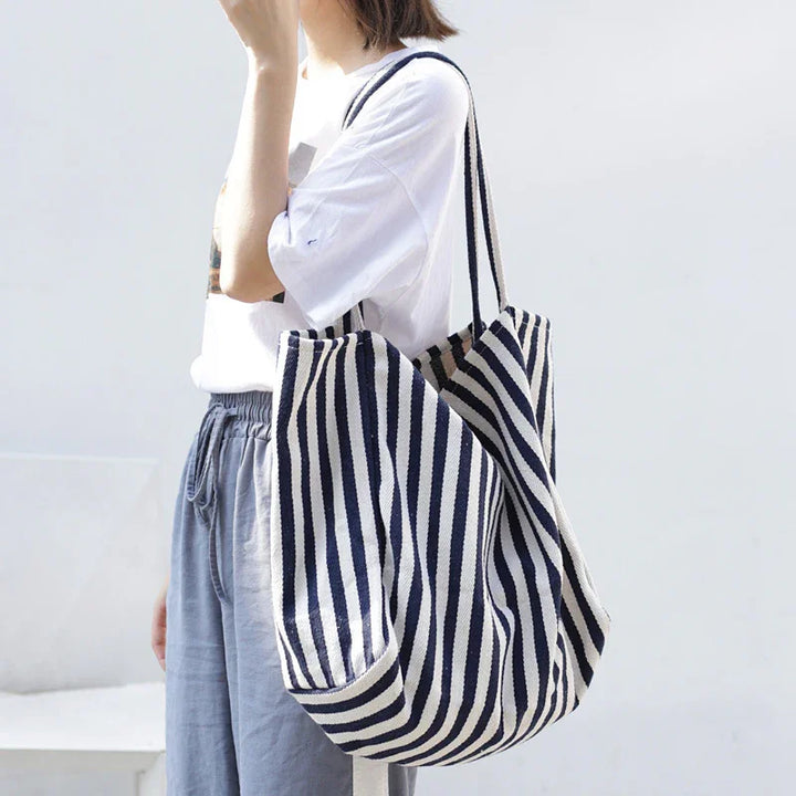 Woman wearing casual white t-shirt and gray pants carrying large navy and white striped tote bag