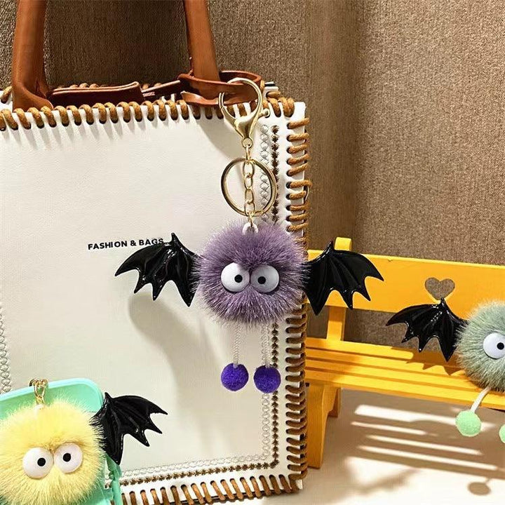 Cute fluffy keychains with bat wings and big eyes hanging on bags and yellow wooden bench