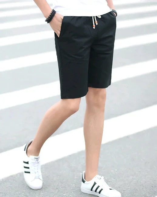 Person wearing black casual shorts and white sneakers with black stripes walking on a crosswalk