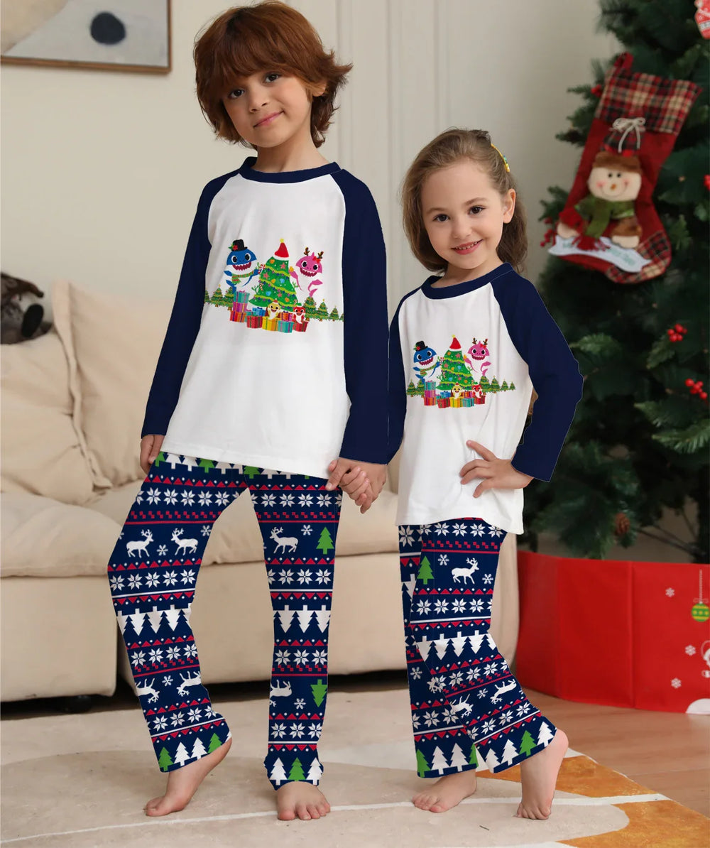 Two children wearing matching Christmas pajamas with holiday tree and reindeer pattern, standing by decorated Christmas tree