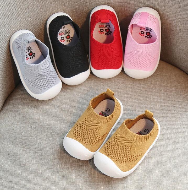 Soft knit baby shoes in gray, black, red, pink, and yellow on a beige fabric surface