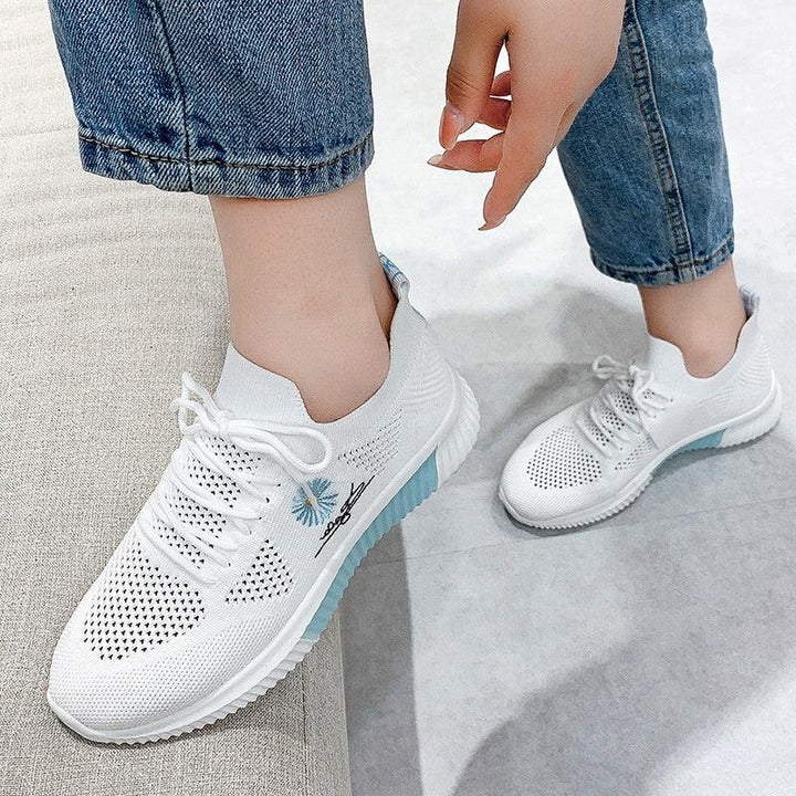 White knitted casual sneakers with blue accents and floral embroidery worn with blue jeans