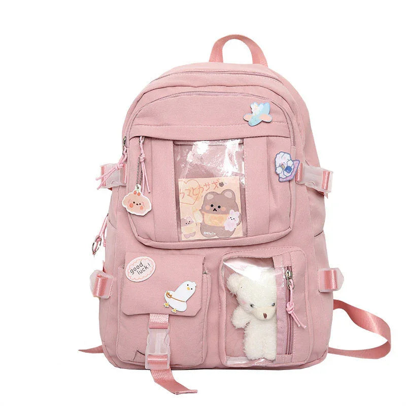 Pink backpack with clear pockets showing a bear card and a small white teddy bear, decorated with cute animal pins