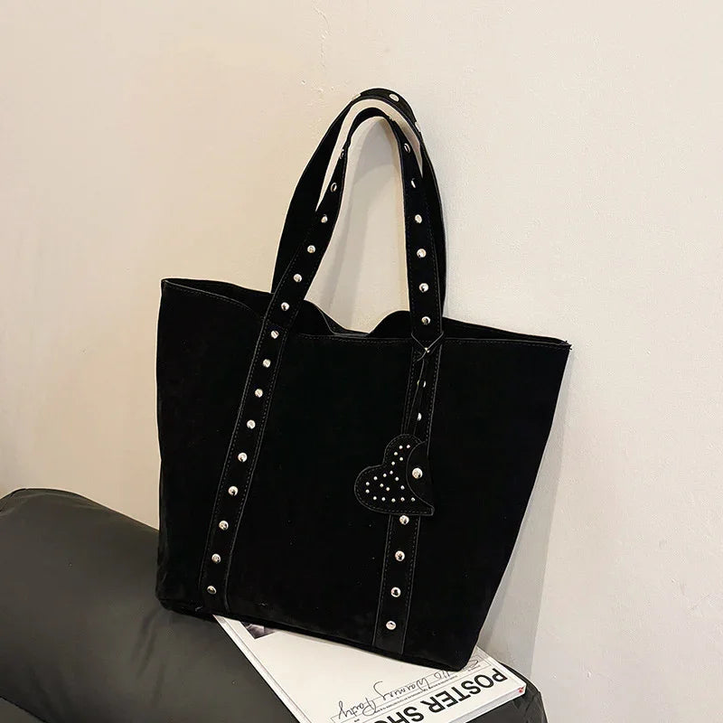 Black tote bag with studded handles and heart-shaped charm, placed on black leather surface and magazine