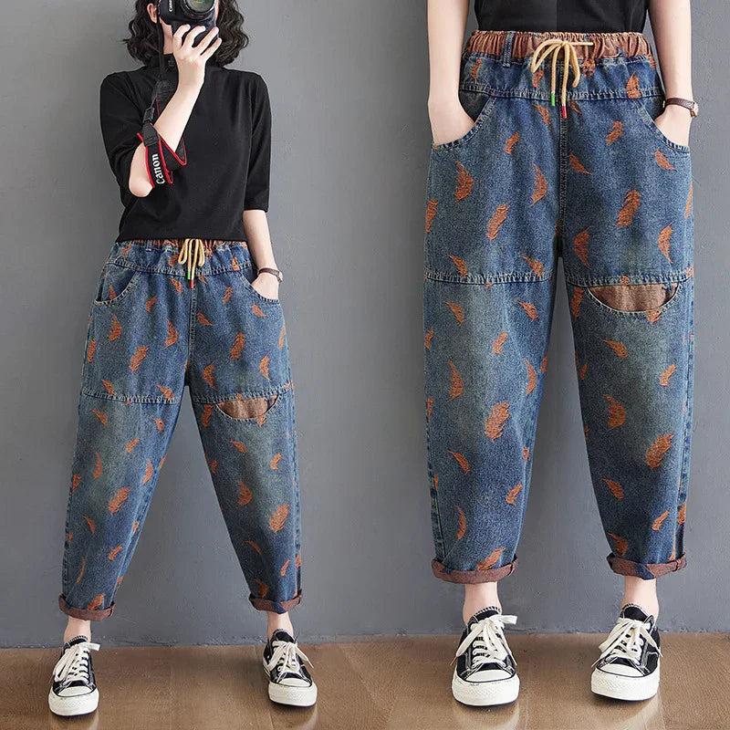 Woman wearing loose denim jogger pants with orange feather print and rolled cuffs, paired with black top and sneakers