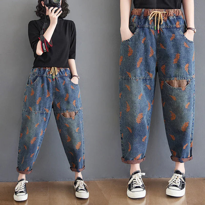 Woman wearing loose denim jogger pants with orange feather print and rolled cuffs, paired with black top and sneakers