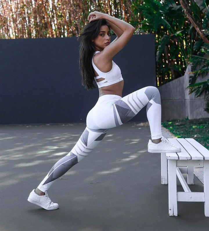 Woman stretching outdoors wearing white and gray leggings with patterned design and white sports bra