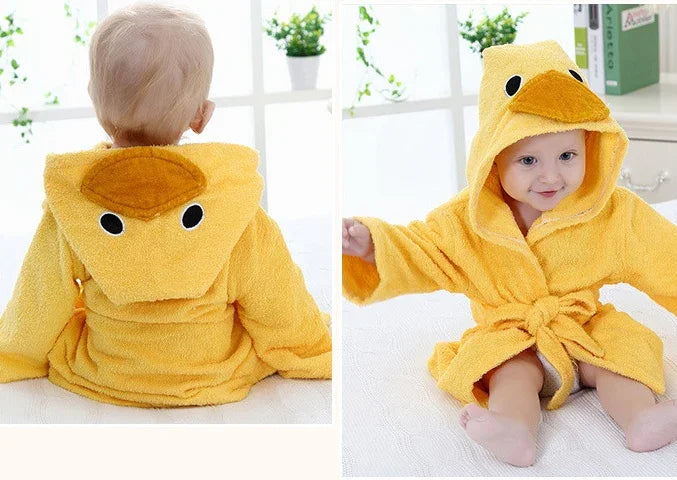 Baby wearing a soft yellow duck-themed hooded robe with beak and eyes in a bright room