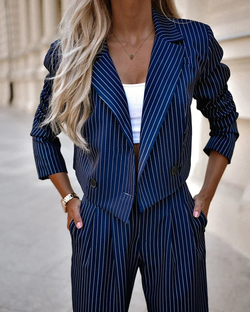 Woman wearing navy pinstripe blazer and matching trousers with a white crop top and gold watch