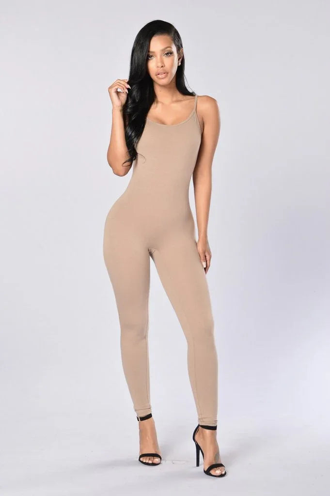 Woman in fitted beige jumpsuit and black heels posing on plain light background