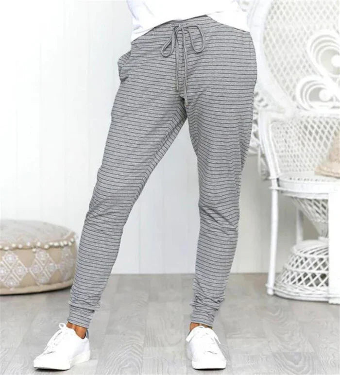Person wearing gray striped jogger pants with drawstring and white sneakers in modern room