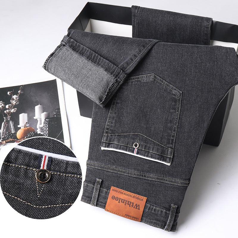 Folded black denim jeans with brown leather Whintloe brand label and detailed stitching on white background