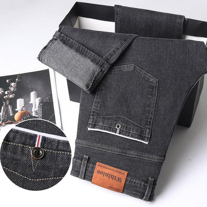 Folded black denim jeans with brown leather Whintloe brand label and detailed stitching on white background