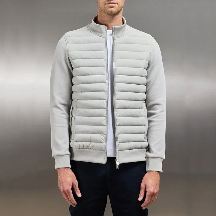 Man wearing light gray quilted bomber jacket with ribbed cuffs over white shirt against gray background