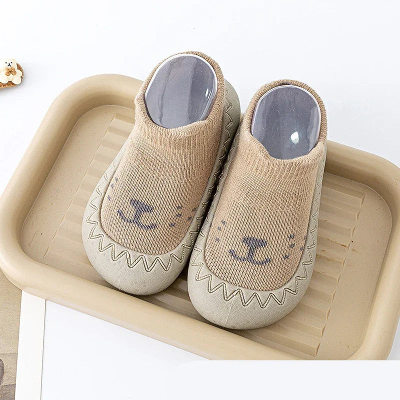 Beige toddler slippers with cute animal face design on a beige tray