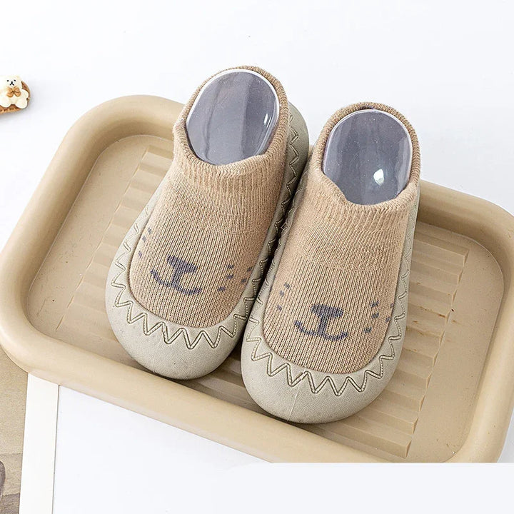 Beige toddler slippers with cute animal face design on a beige tray