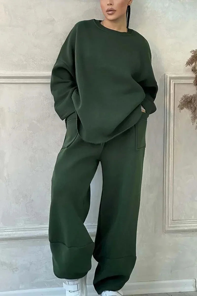 Woman wearing dark green oversized sweatshirt and pants with white sneakers in minimalist room
