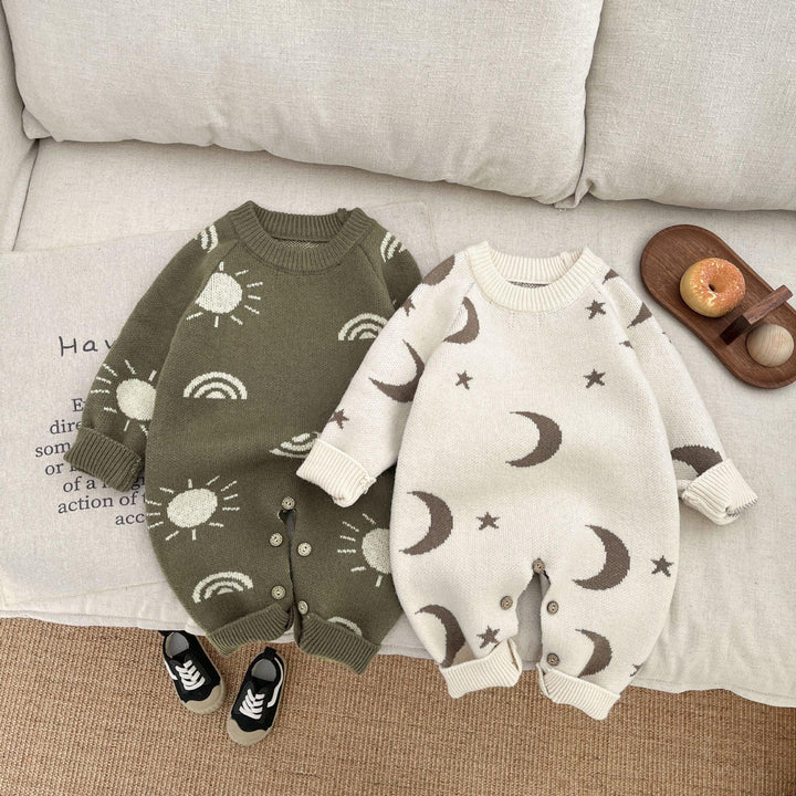 Two knitted infant rompers with sun and moon patterns on beige sofa, black baby shoes nearby