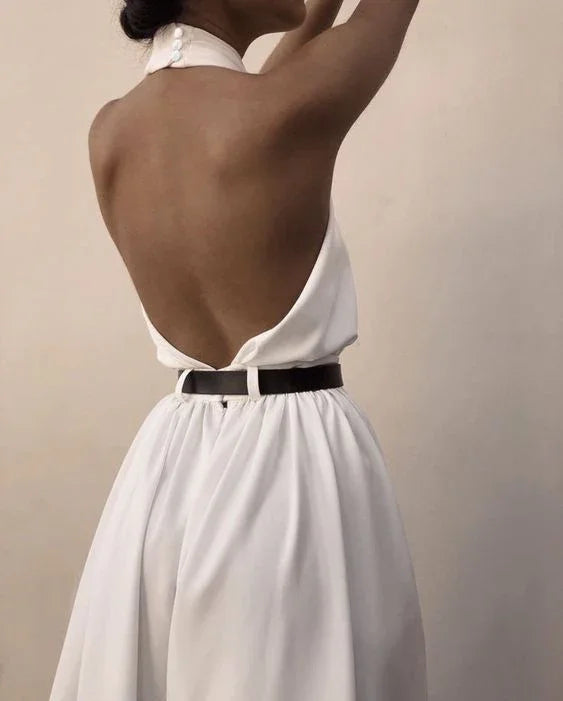 Woman wearing elegant white open-back halter dress with black belt against plain background