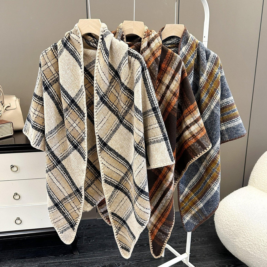 Three plaid poncho capes in beige, brown, and blue hanging on wooden hangers in modern room