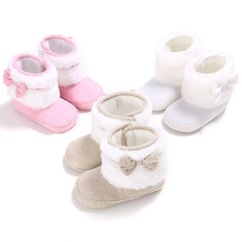 Three pairs of soft baby booties in pink, beige, and white with faux fur cuffs and decorative bows