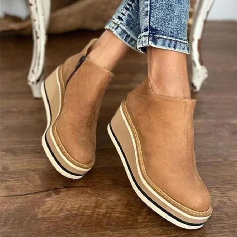 Tan suede wedge platform boots with side zipper worn with rolled-up blue jeans on wooden floor
