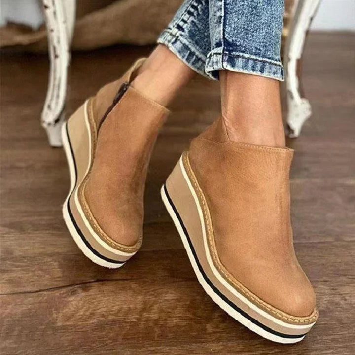 Tan suede wedge platform boots with side zipper worn with rolled-up blue jeans on wooden floor