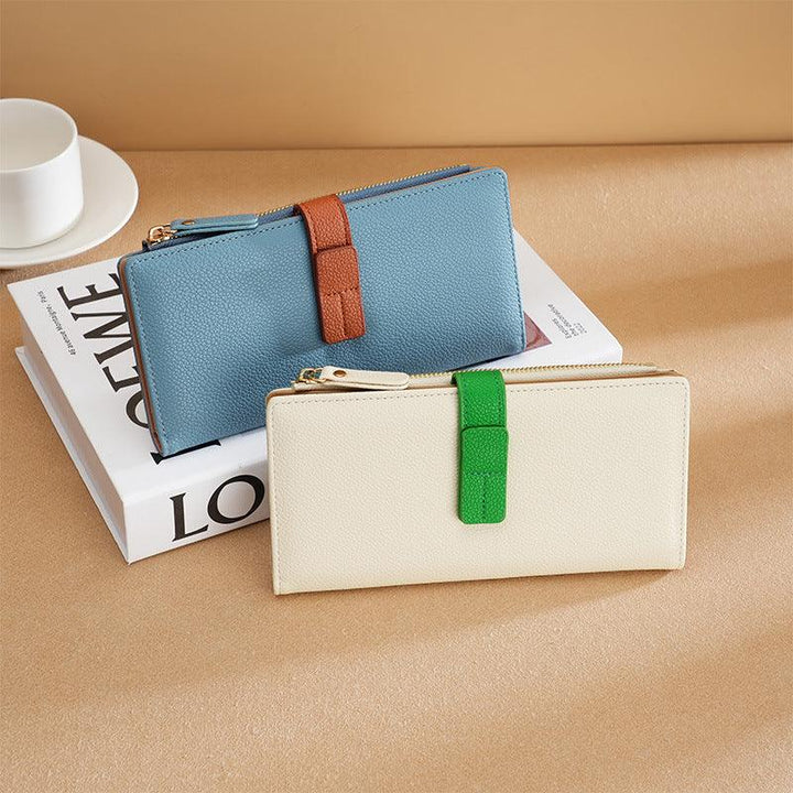 Two textured leather wallets in cream with green strap and blue with brown strap on a book and beige surface