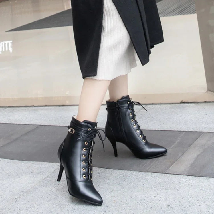 Woman wearing black lace-up high-heeled ankle boots with gold eyelets on sidewalk