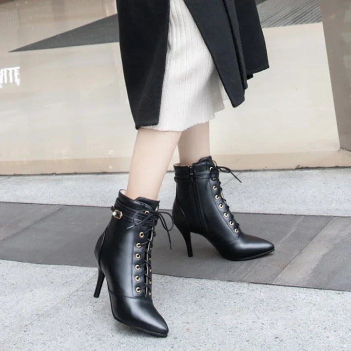 Woman wearing black lace-up high-heeled ankle boots with gold eyelets on sidewalk