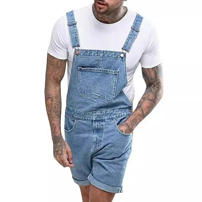 Man wearing blue denim short overalls with front pocket over white t-shirt, visible arm tattoos
