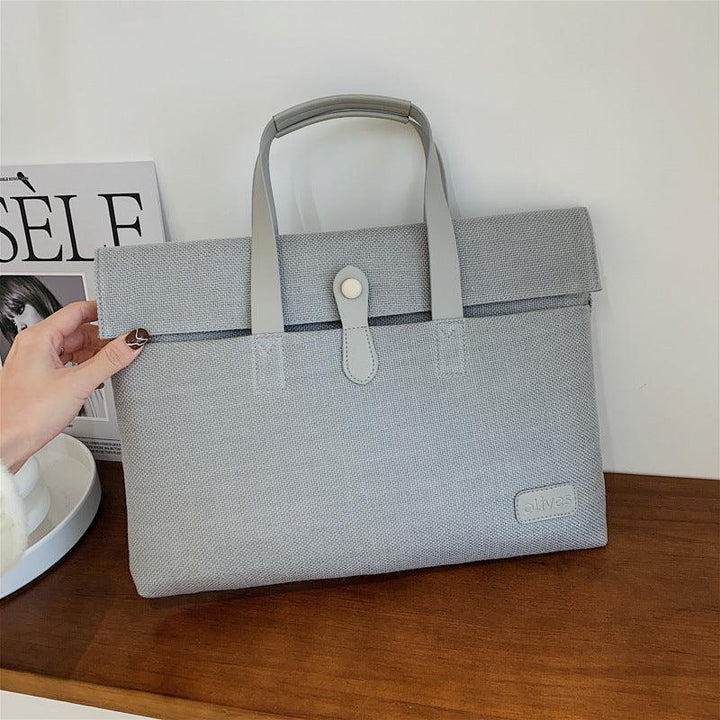 Light gray fabric tote bag with handles and button closure on wooden surface, stylish minimal design