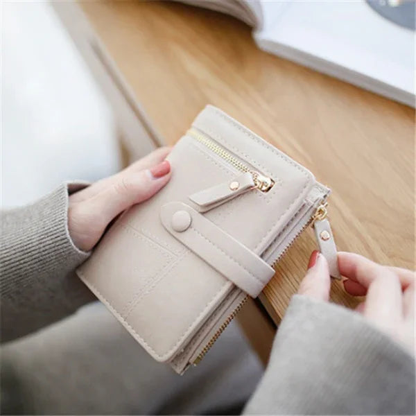 Hands holding a beige leather wallet with gold zipper and snap button on wooden table