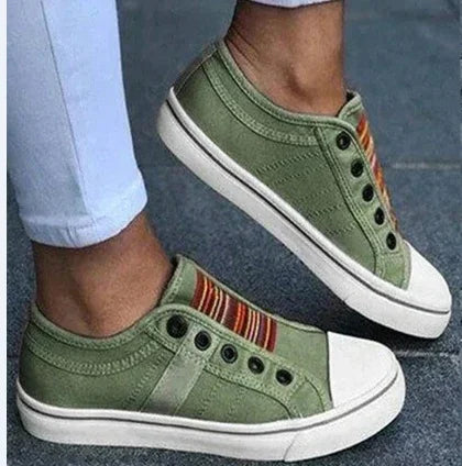 Green canvas slip-on sneakers with white rubber toe caps and striped fabric detail worn with white pants