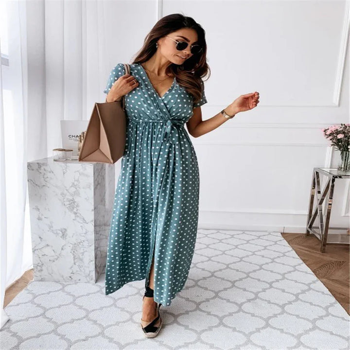 Woman wearing blue polka dot maxi dress with tie waist, sunglasses, carrying beige handbag indoors