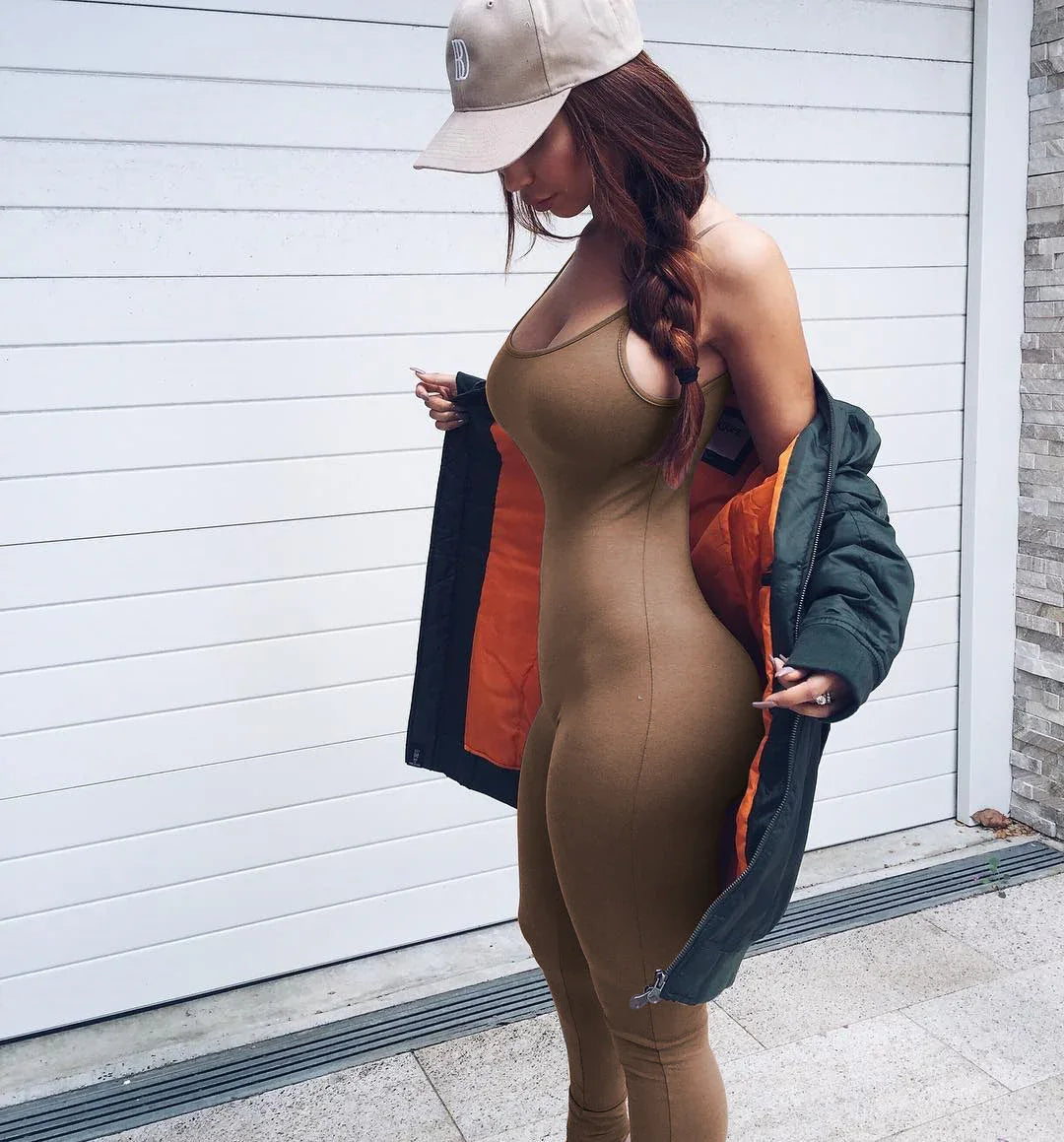 Woman in tan jumpsuit, green jacket, and beige cap posing outdoors by a white garage door